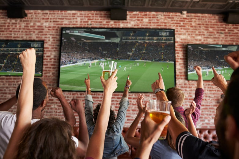Patrons of a bar hold up beers as the watch a soccer game.